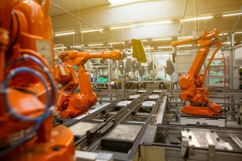 Industrial orange robotic arms working on automated assembly line in a bright factory setting.