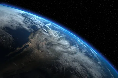 View of Earth from space showing atmosphere, clouds, landmasses, and the dark starry background of outer space.