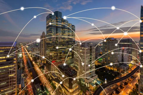 City skyline at sunset with interconnected digital network lines symbolizing smart technology and communication.
