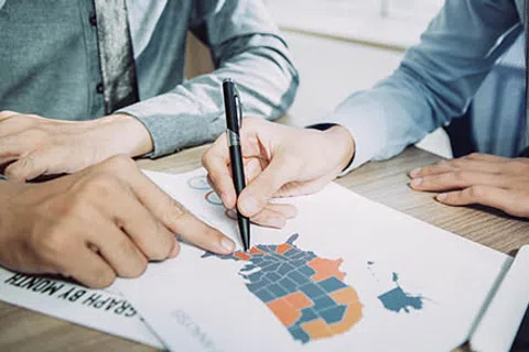 Two people reviewing a color-coded regional map on paper at a desk in a business meeting.