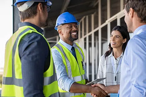 Construction workers and project managers shaking hands and discussing plans at a building site.
