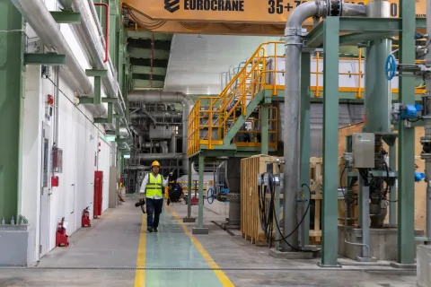 Employee walking through manufacturing plant with safety vest and hard hat on.