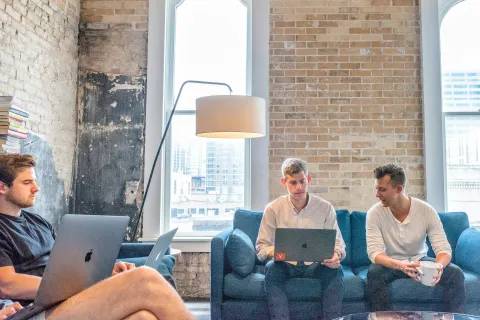 men sitting on a couch using laptops