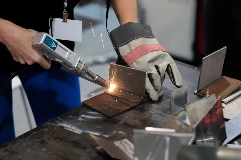 Close-up of a worker welding metal pieces with protective gloves and sparks flying on a workbench.