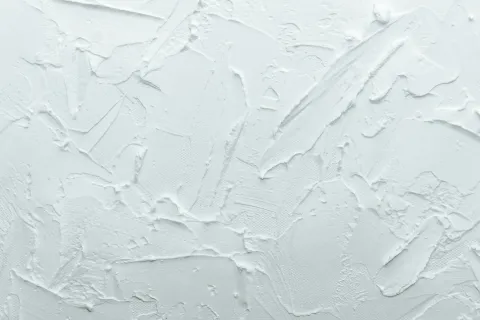 White textured plaster wall with rough, uneven patterns and brush strokes creating a 3D effect.
