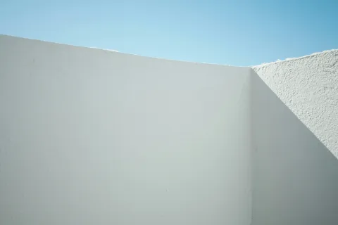 Minimalist white stucco walls casting sharp shadows under a clear blue sky on a sunny day