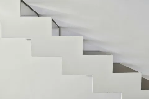 Minimalist white zigzag staircase against a plain light gray wall in modern interior design