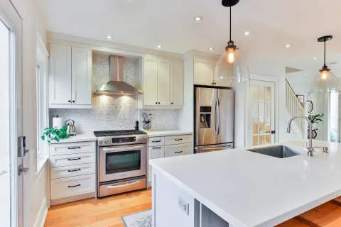Bright modern kitchen with white cabinets, stainless steel appliances, large island, and pendant lights.