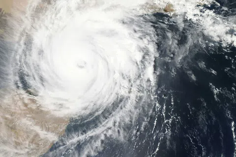 Satellite image of a large hurricane forming over the ocean near a desert coastline with a visible eye.