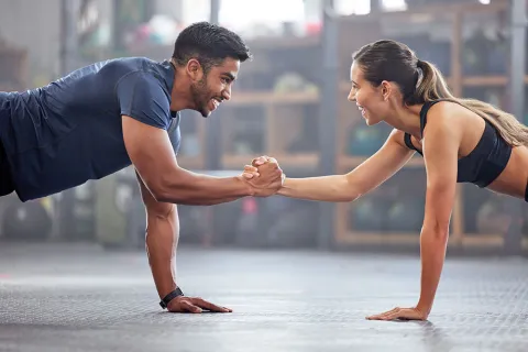 Man and woman doing plank exercise while shaking hands, smiling and working out together indoors.