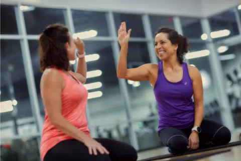 Two women in workout clothes giving a high five during a fitness session at the gym.