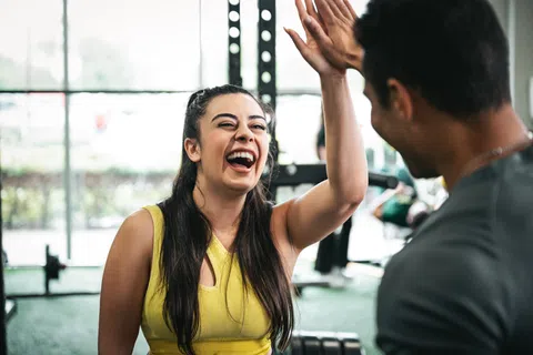 Smiling woman in yellow tank top giving a high five to a man at the gym.