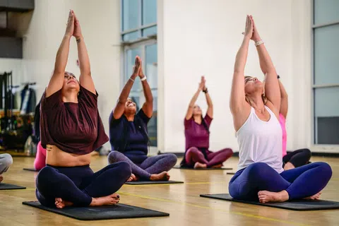 Group of women practicing seated yoga with arms raised in a bright studio