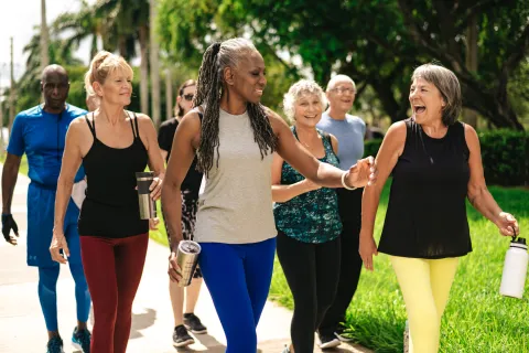 Group of diverse seniors happily walking outdoors in activewear holding water bottles and chatting.