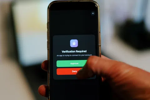 Smartphone screen showing verification required prompt with approve and deny buttons being pressed by a hand.