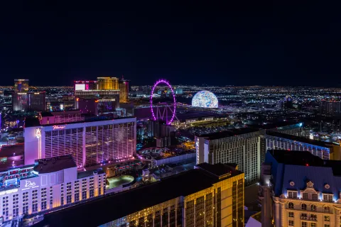 Night aerial view of Las Vegas Strip featuring illuminated hotels, High Roller Ferris wheel, and vibrant city lights.