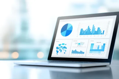 Laptop screen displaying various blue charts and graphs including pie chart, bar charts, and world map analytics.