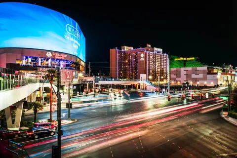 Busy Las Vegas intersection at night with light trails, bright billboards, and illuminated casino buildings.
