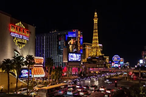 Night view of Las Vegas Strip with illuminated casinos, Eiffel Tower replica, and busy traffic under dark sky.