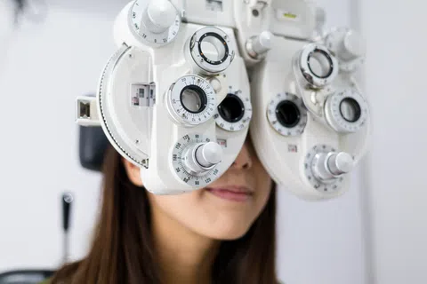 Close-up of a woman undergoing an eye exam with a phoropter device in an optometrist office.