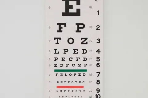 Eye chart with black letters and colored lines for vision testing against a plain white wall.