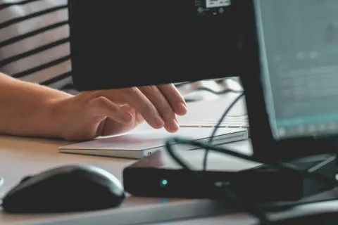 Person using a laptop keyboard on a desk surrounded by computer mouse and monitors in a workspace.