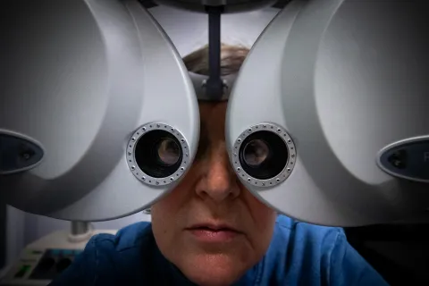 Middle-aged person undergoing eye exam with a phoropter device in an optometry clinic.