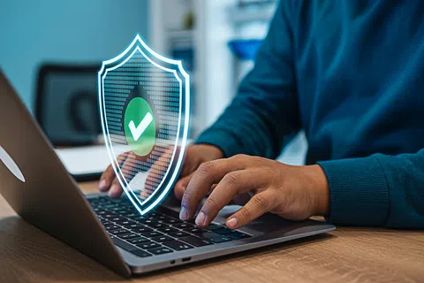 Person typing on laptop with a shield and checkmark symbolizing online security and data protection.