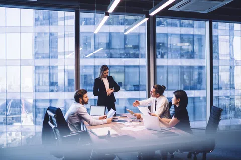 Business team collaborating in a modern glass office during a daytime meeting with laptops and documents.