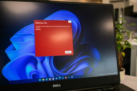 Dell laptop screen displaying a red warning about a malicious file with a blue abstract Windows background.