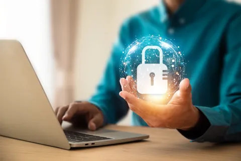 Person holding digital padlock hologram over laptop symbolizing data security and cyber protection.