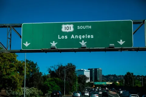 Highway 101 South green road sign directing traffic towards Los Angeles on a sunny day with cars below.