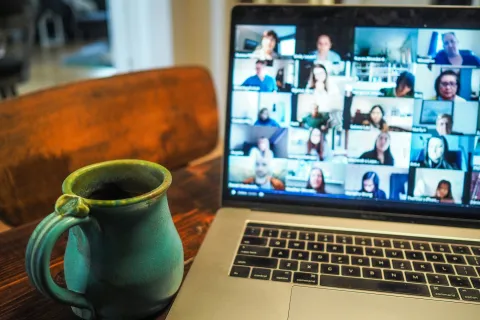 Green ceramic mug beside a laptop displaying a virtual group video meeting on a wooden table indoors.