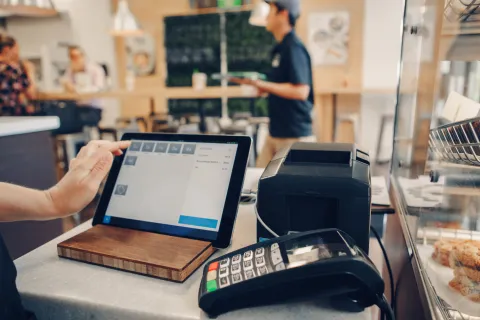 Point of sale tablet and payment terminal on cafe counter with blurred staff and customers in background