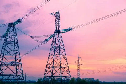 High-voltage power lines and tall transmission towers against a pink and orange sunset sky