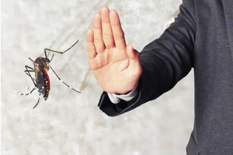 Person in suit holding hand up to stop a mosquito flying nearby against light background