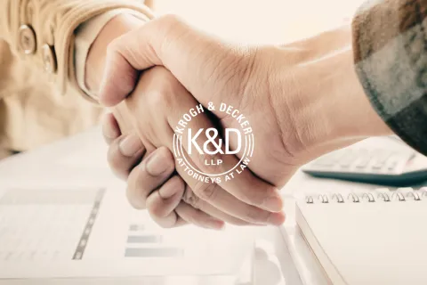 Two people shaking hands over documents, paper, and a notebook in a professional setting with K&D attorneys logo.
