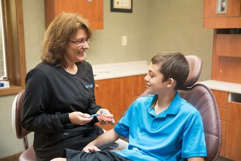 Dental hygienist smiling and showing a dental model to a boy in a clinic celebrating National Dental Hygiene Month.