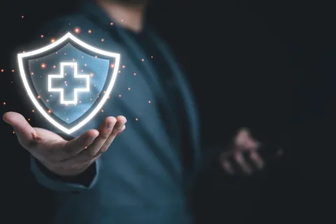 Person holding a glowing shield with a medical cross symbol representing healthcare protection and security.
