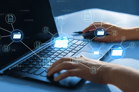 Hands typing on a laptop keyboard with digital folder and file icons representing data management and networking
