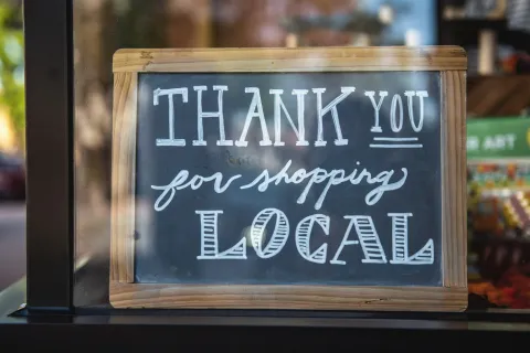 Chalkboard sign with wooden frame reading Thank You for Shopping Local in a shop window.