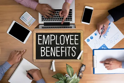 Top view of business team working around chalkboard with employee benefits text and office tools on table