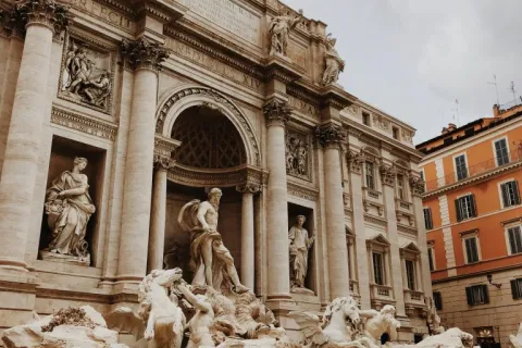a large stone building with statues with Trevi Fountain in the background