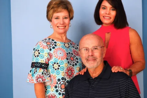 Smiling elderly man with two women standing behind him against a blue background