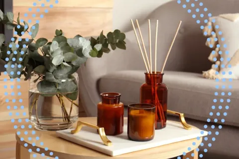 Brown glass jars and candle with reed diffuser on tray beside eucalyptus bouquet on wooden table.