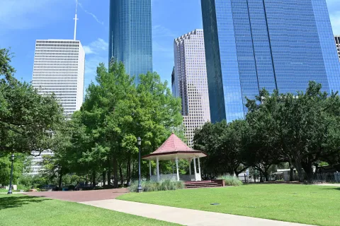 Urban park gazebo surrounded by green trees with skyscrapers in the background on a clear day