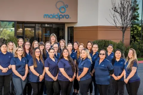 Group of MaidPro cleaning staff in navy uniforms posing outside the MaidPro office building with logo visible.