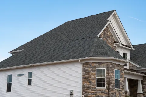 Modern house exterior with gray roofing, stone facade, white siding, and clear blue sky background
