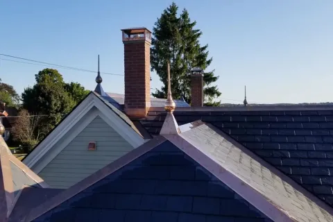 Slate roof with decorative finials and brick chimneys on residential houses under clear blue sky.