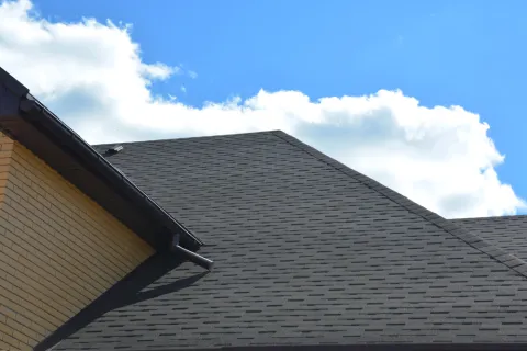 Close-up of a modern house roof with dark asphalt shingles under a blue sky with white clouds